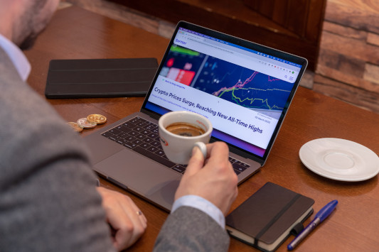 Man sitting at laptop holding a coffee while looking at financial market data